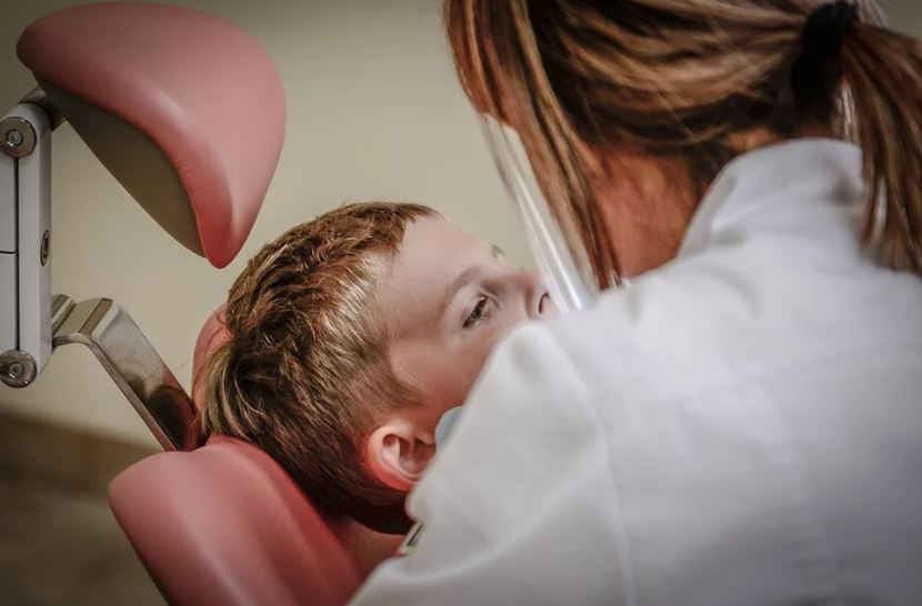 pink dental chair, dentist with a blonde hair, boy laying down the chair